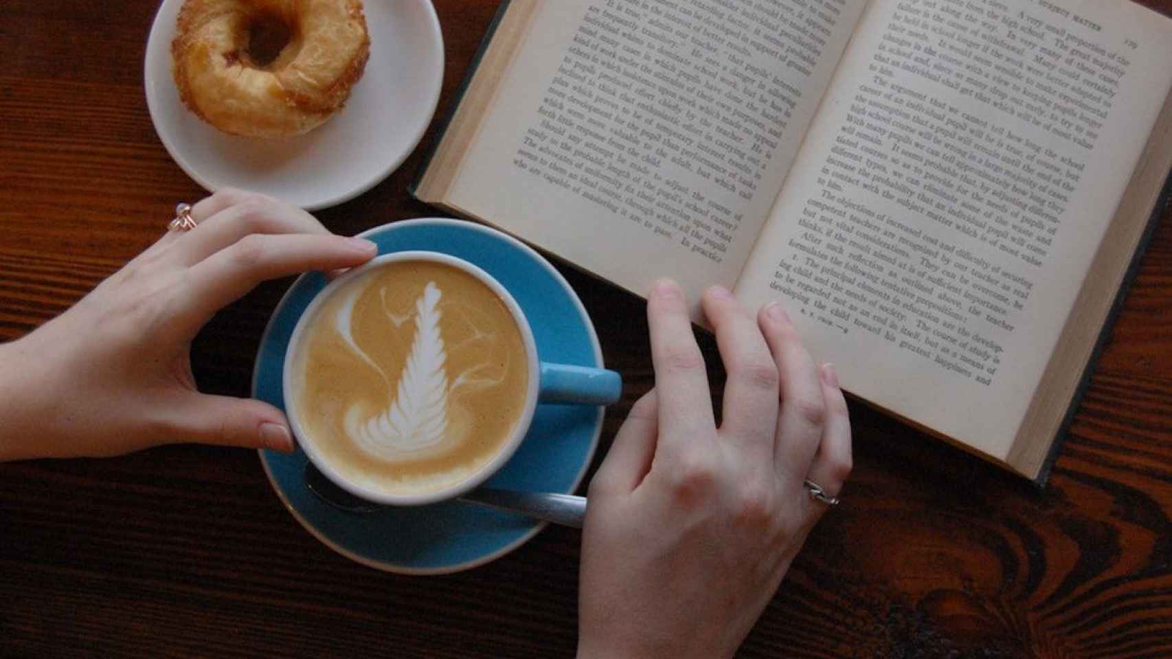 Una persona tomando un café y leyendo un libro / UNSPLASH