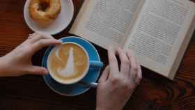 Una persona tomando un café y leyendo un libro / UNSPLASH