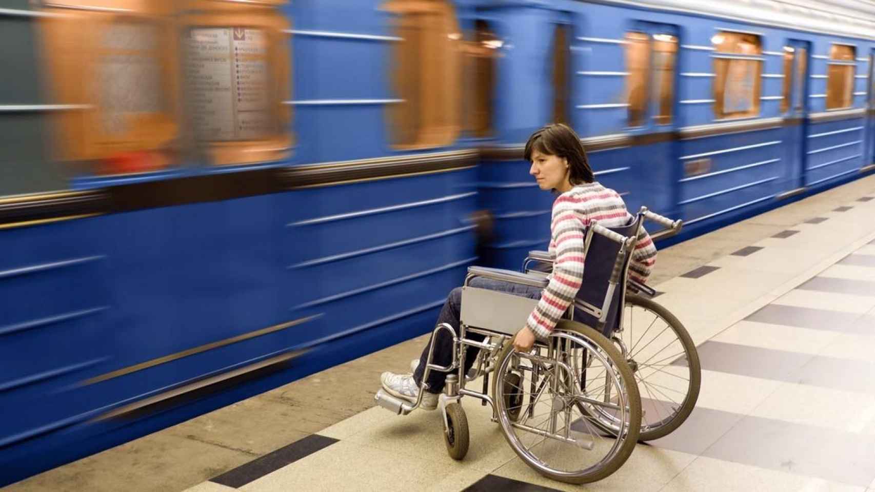 Una mujer en silla de ruedas frente a un convoy de metro en funcionamiento