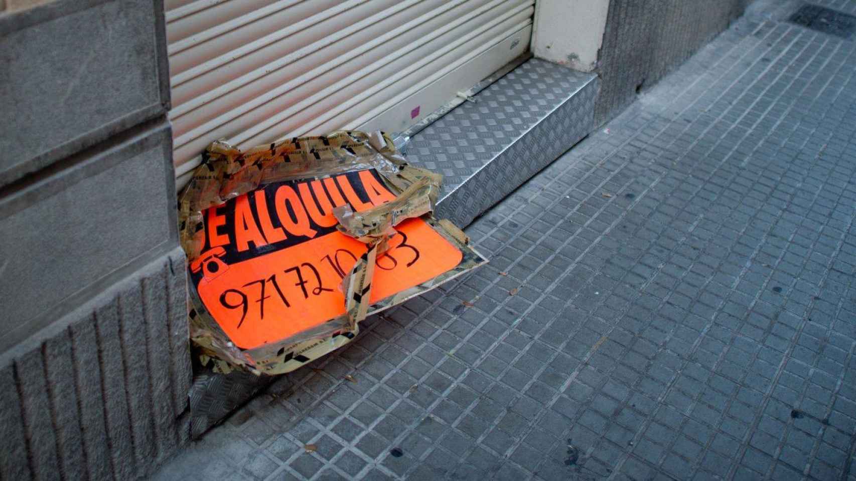 Un cartel de 'se alquila' roto y descolgado en el suelo de Barcelona