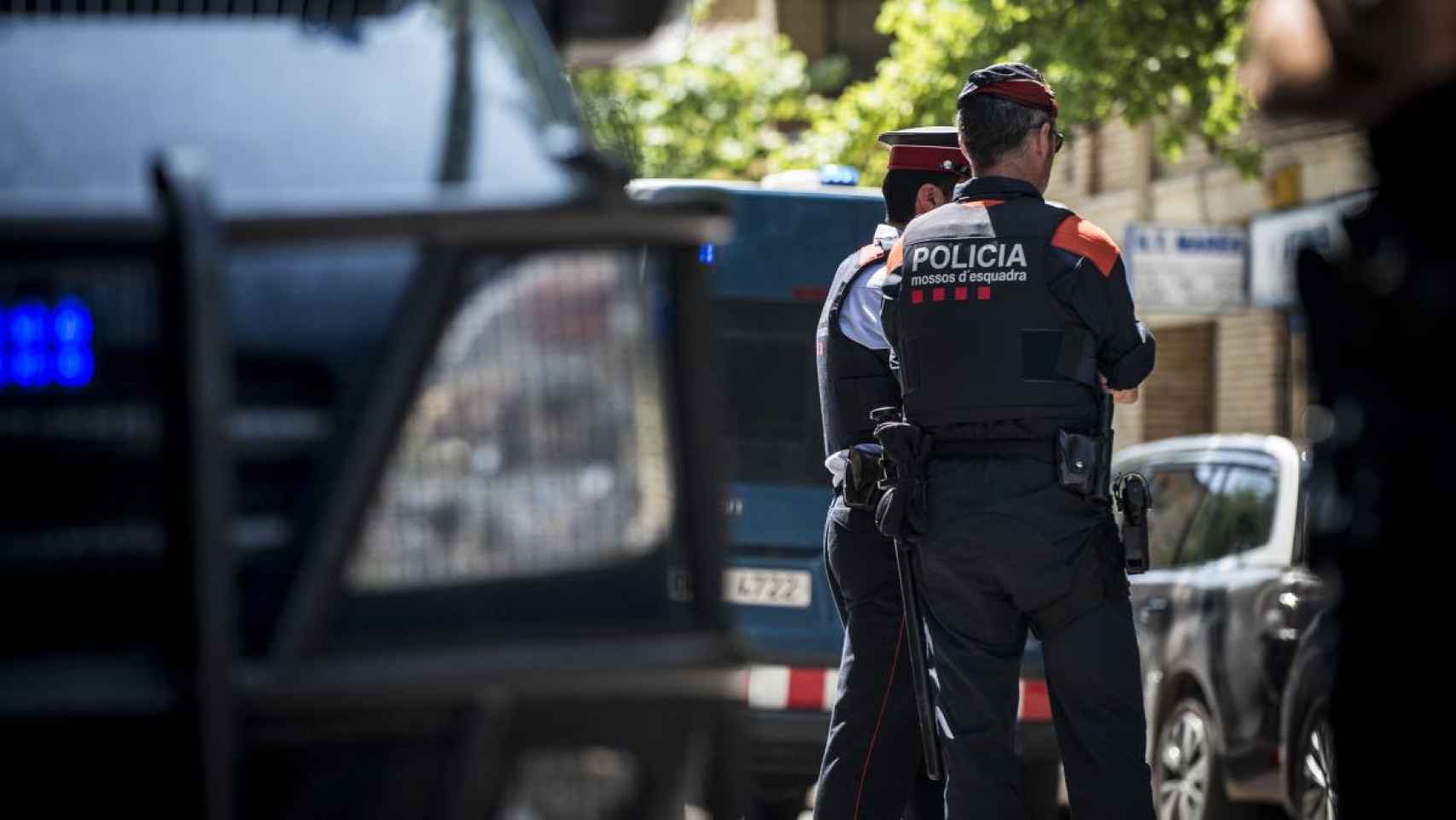 Dos agentes de los Mossos d'Esquadra junto a varios coches policiales