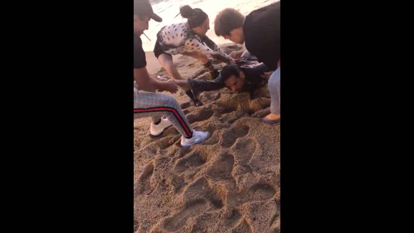 Tres personas ayudan a sacar al hombre, inconsciente, del agua en la playa de la Barceloneta