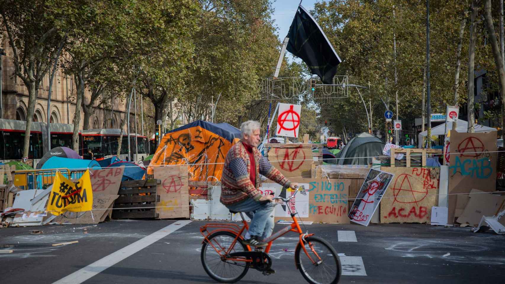 Un hombre en bicicleta detrás de las tiendas de campaña de plaza Universitat / EP