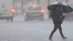 Una persona cruza una calle un día de lluvia en Barcelona / EFE