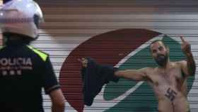 Un joven ultra, con un esvástica en el pecho, hace la peineta ante un agente de policía