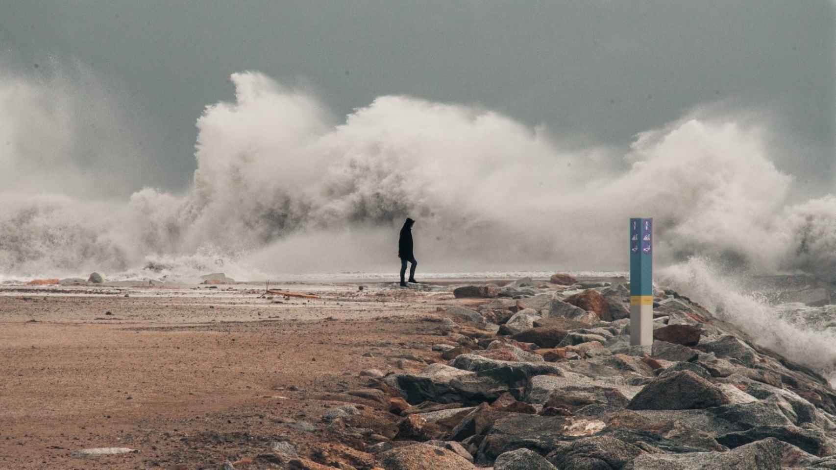 Un hombre al lado de una gigante ola en la playa de Barcelona