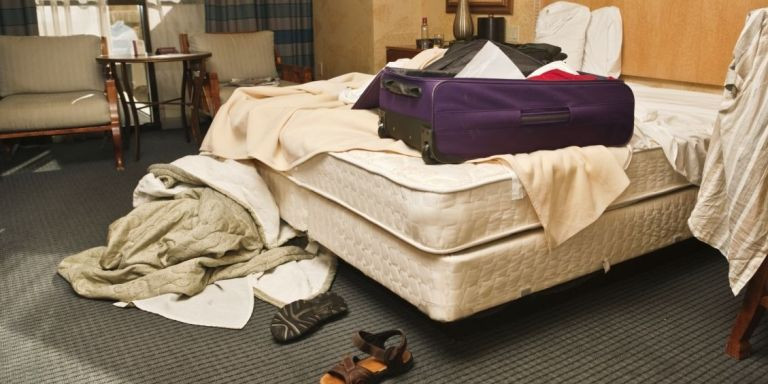 Habitación de hotel llena de ropa y la cama sin hacer