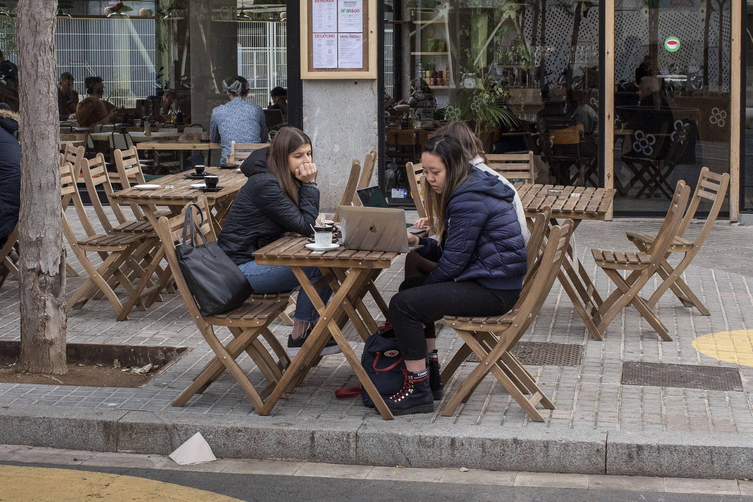Tres chicas consultan un ordenador portátil mientras se toman un café en un restaurante vegano / Lena Prieto