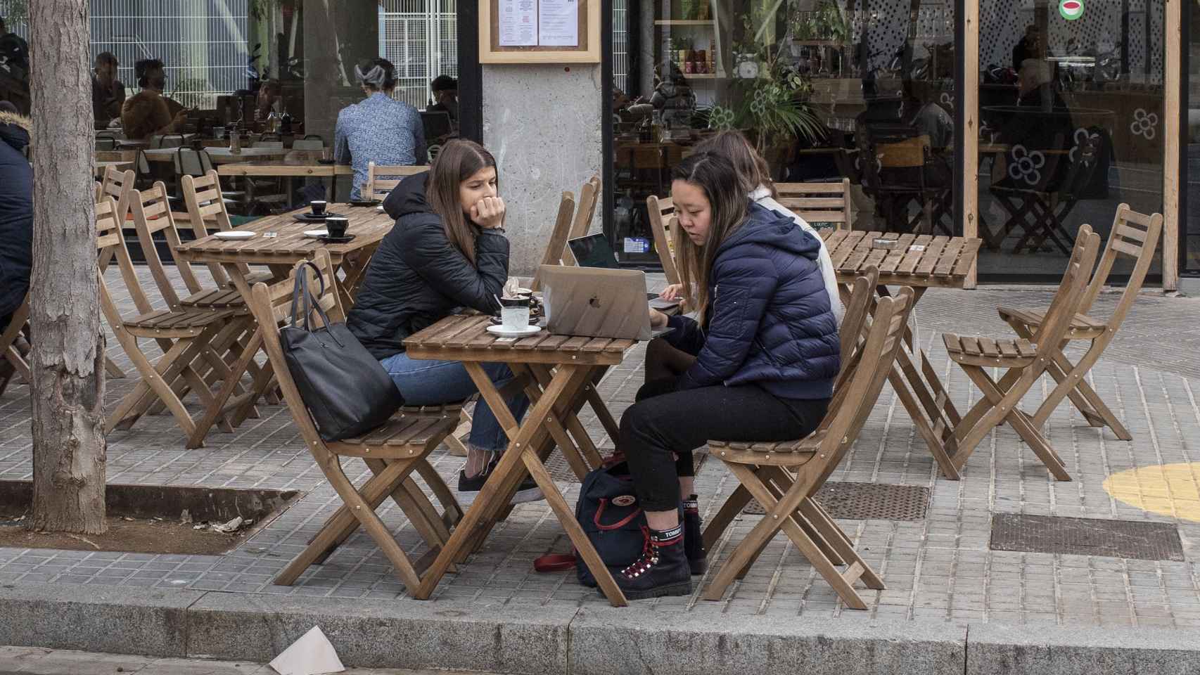 Tres chicas consultan un ordenador portátil mientras se toman un café en un restaurante vegano / Lena Prieto