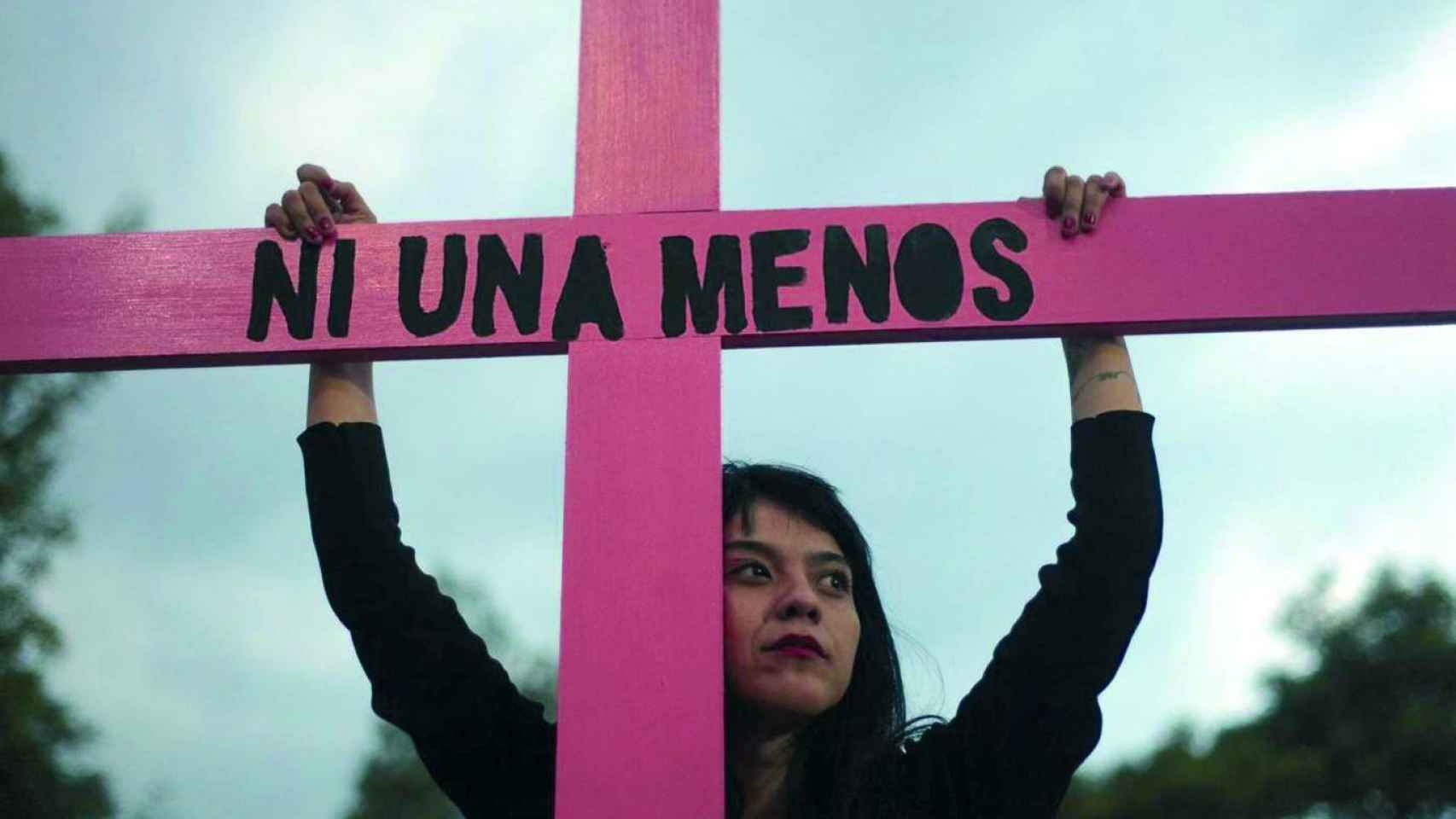 Una joven sujeta una cruz de color rosa durante una concentración contra la violencia machista / EFE
