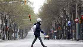 Un motorista con mascarilla cruza una calle vacía del barrio de Sants