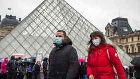 Personas con mascarillas gratuitas que han sido repartidas entre los ciudadanos de París en la pirámide del museo del Louvre
