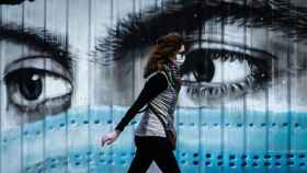 Una mujer camina ante un grafiti en Barcelona / EFE - ENRIC FONTCUBERTA
