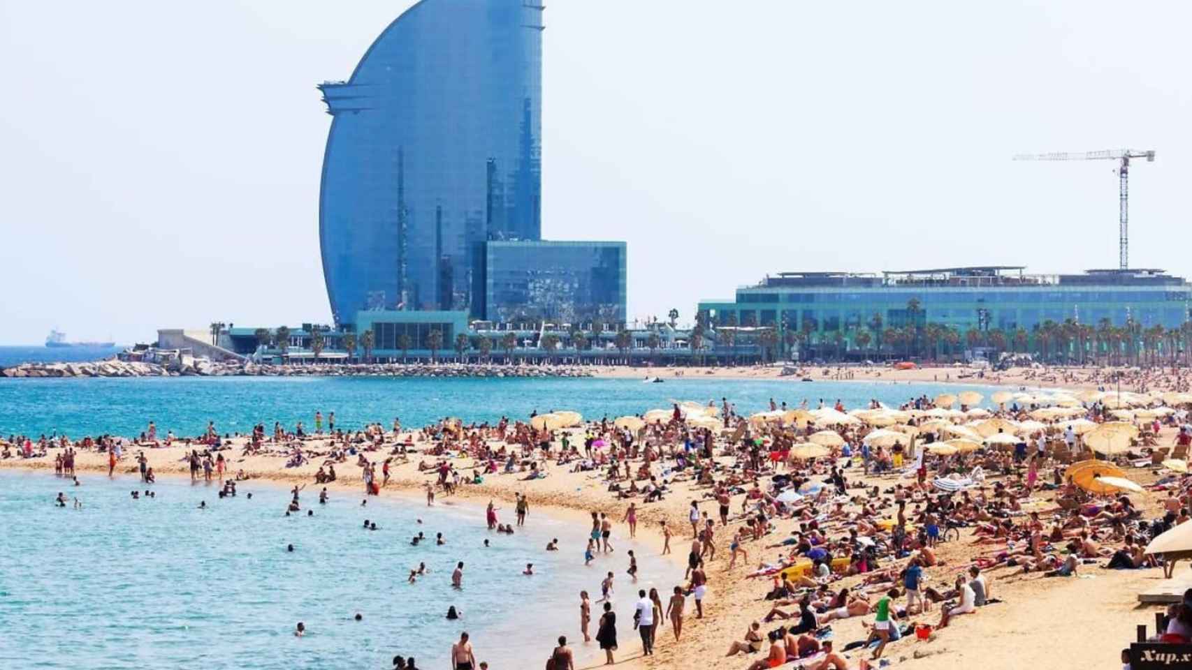 La playa de la Barceloneta con multitud de gente y el hotel W de fondo