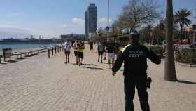 Un guardia urbano para a unos turistas en las playas de Barcelona, en marzo / MA