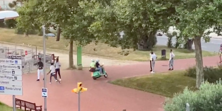 Una moto circula entre jóvenes sin mascarilla por una acera