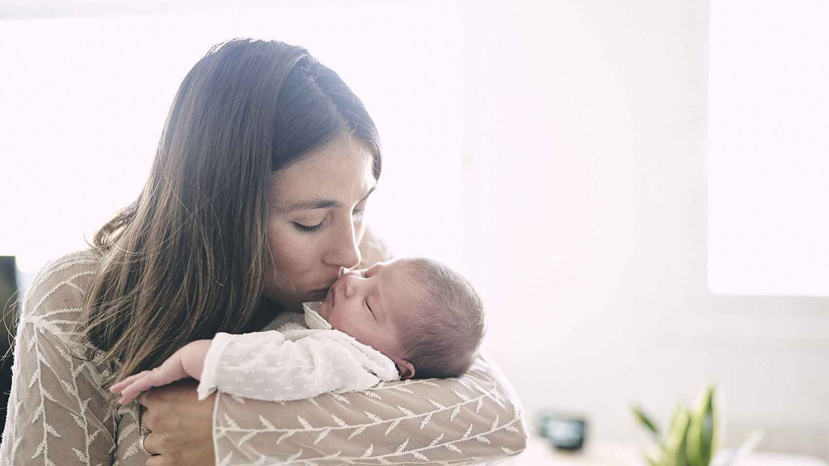 Una madre coge a un bebé en brazos mientras le da un beso