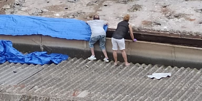 Dos personas colocan una lona de plástico en el tejado de la asociación Blanca Paloma / CEDIDA