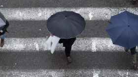 Tres personas cubiertas con un paraguas cruzando por un paso de peatones / EFE