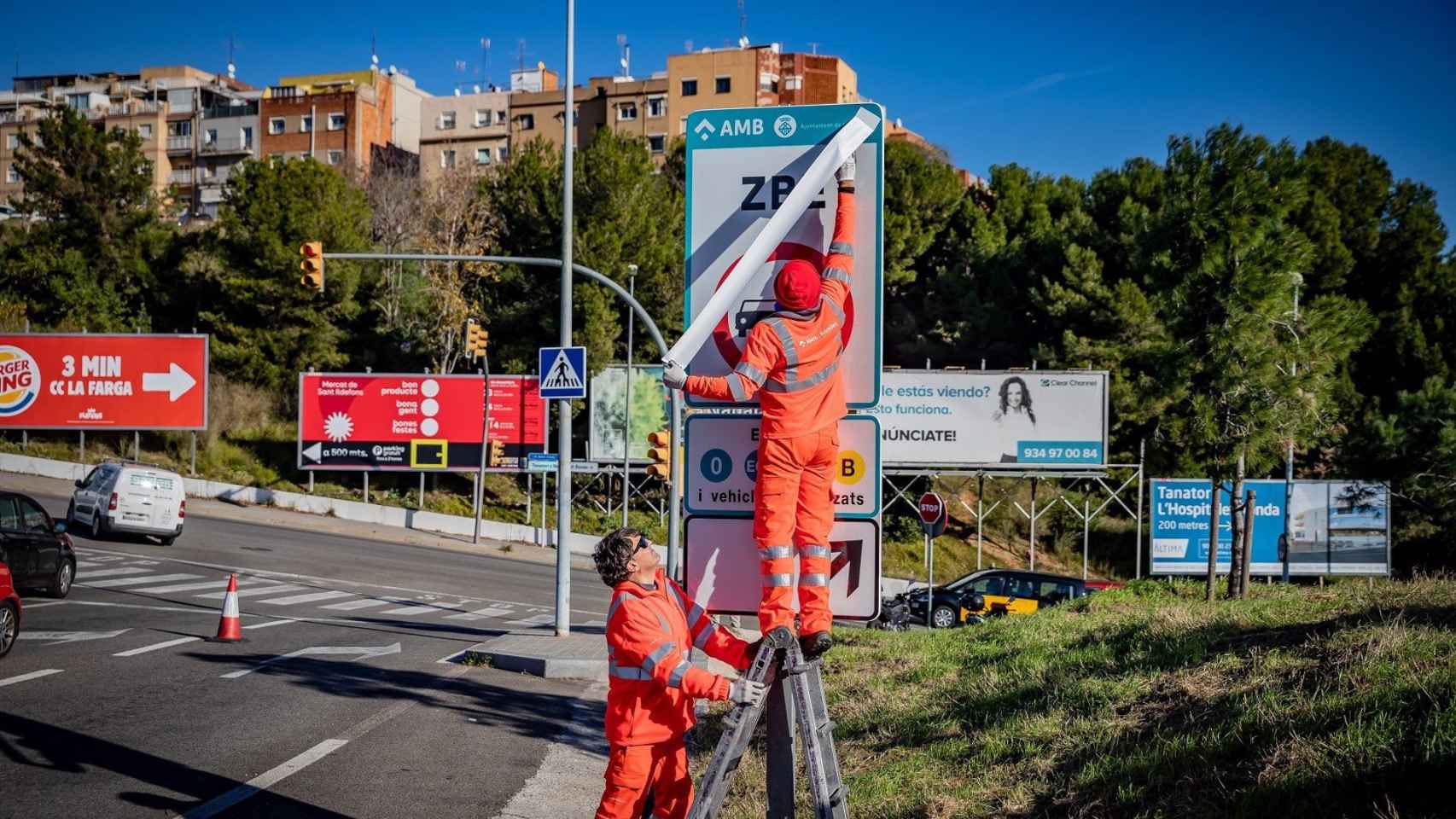 Operarios instalando las señales de tráfico definitivas de la ZBE Rondas BCN en el ramal de la salida 14 Besòs de la Ronda de Dalt, en L'Hospitalet de Llobregat /