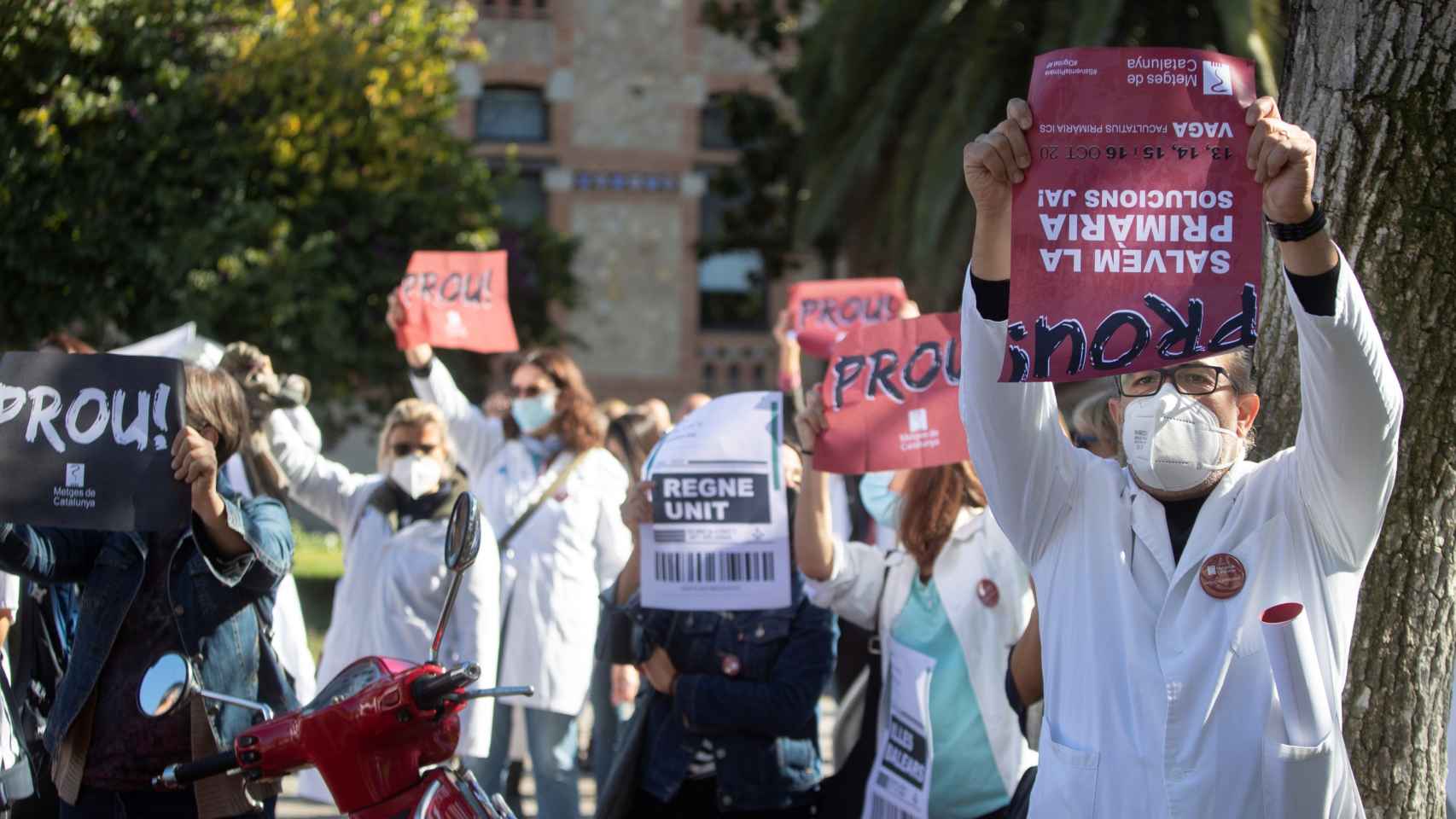 Decenas de médicos de la atención primaria pública protestan con carteles de los destinos a los que tienen que emigrar ante la sede del departamento de Salud en Barcelona /
