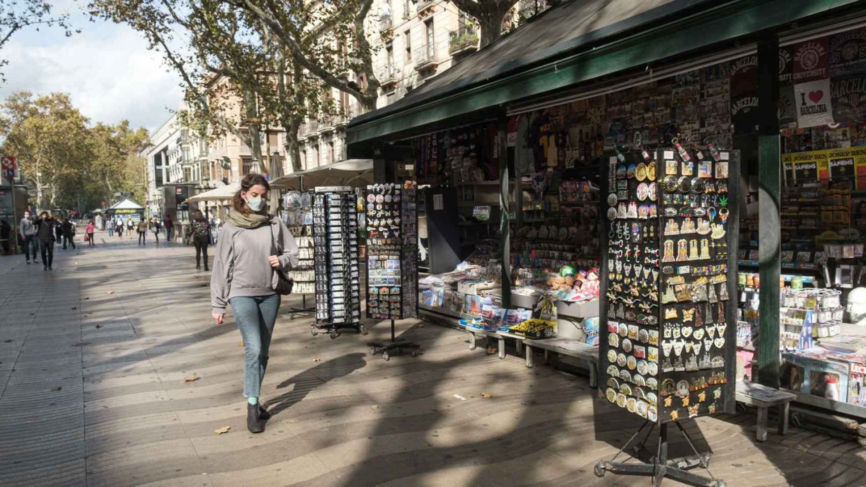 Una mujer camina delante de un kiosko en La Rambla, casi desértica por la ausencia de turistas en Barcelona / CG- PABLO MIRANZO