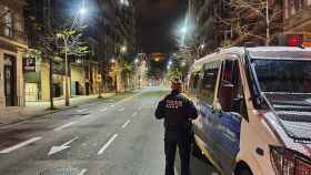Un agente de la Guardia Urbana observa una calle vacía al lado de un furgón policial / AYUNTAMIENTO
