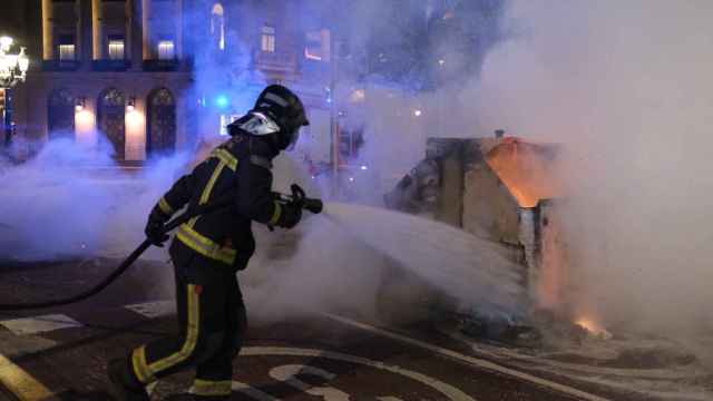 Un contenedor quemado en el centro de Barcelona, apagado por un bombero tras las protestas contra las restricciones / PABLO MIRANZO