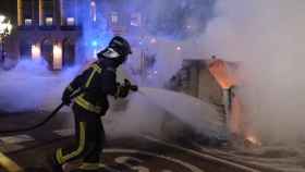 Un contenedor quemado en el centro de Barcelona, apagado por un bombero tras las protestas contra las restricciones / PABLO MIRANZO
