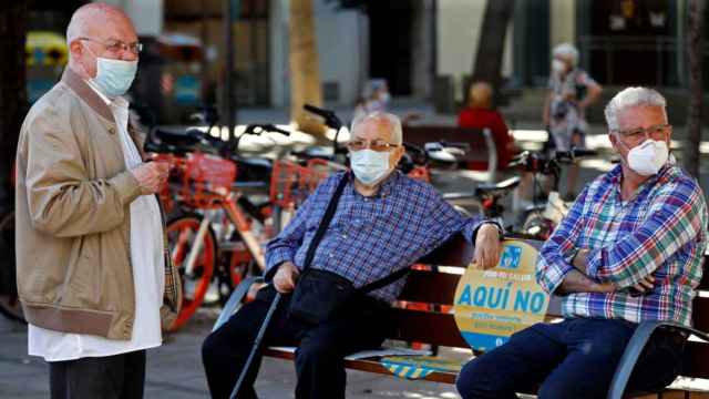 Tres barceloneses sentados tomando la fresca, uno de ellos con la mascarilla mal puesta y la nariz asomando / EFE