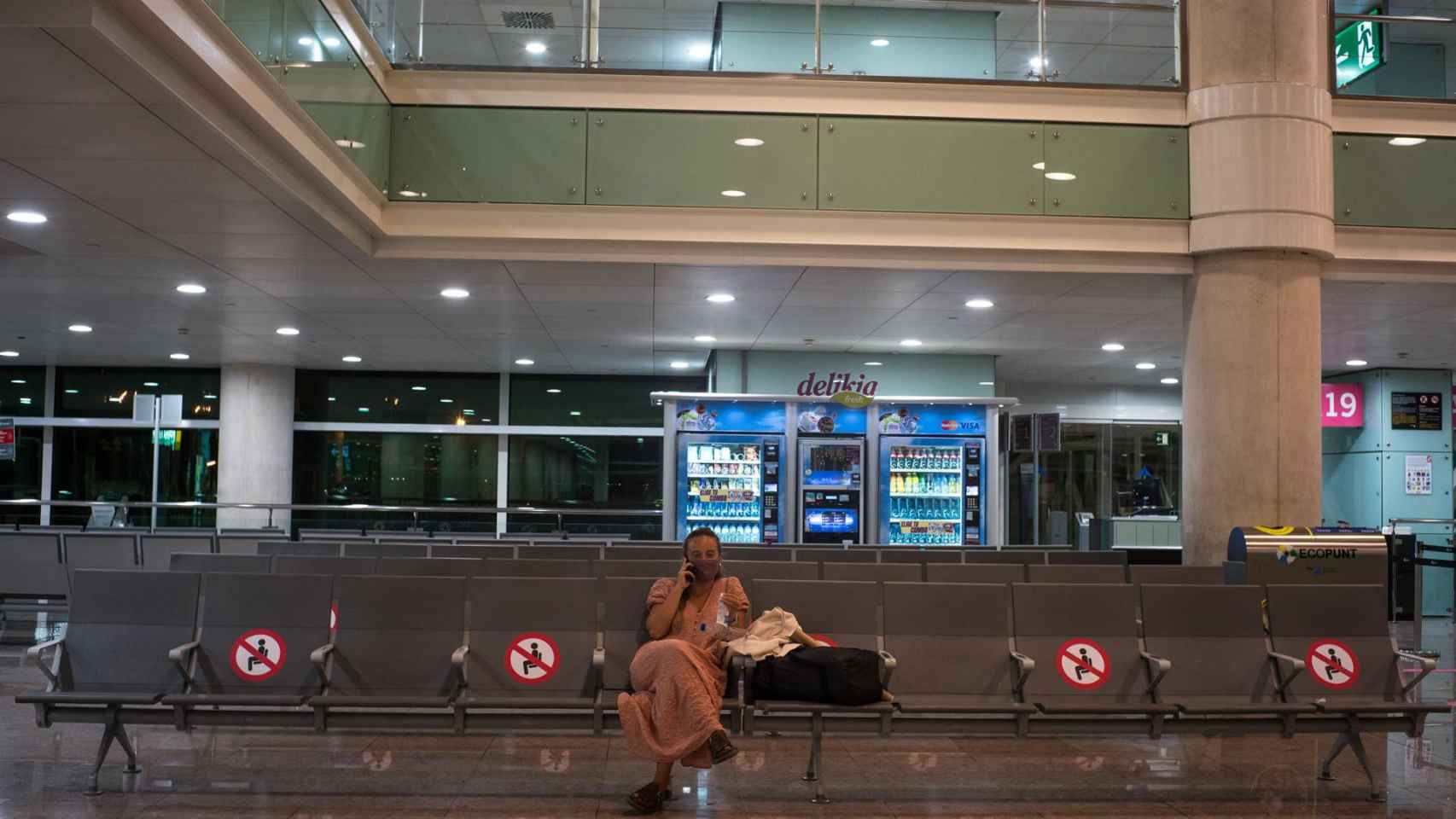 Una mujer espera sentada en unos asientos habilitados para preservar la distancia de seguridad en el Aeropuerto Josep Tarradellas Barcelona-El Prat, en Barcelona / EUROPA PRESS