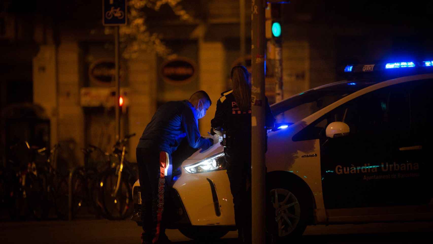 Una persona firmando una denuncia por incumplir las restricciones en el capó de un coche de la Guardia Urbana de Barcelona / EUROPA PRESS - David Zorrakino
