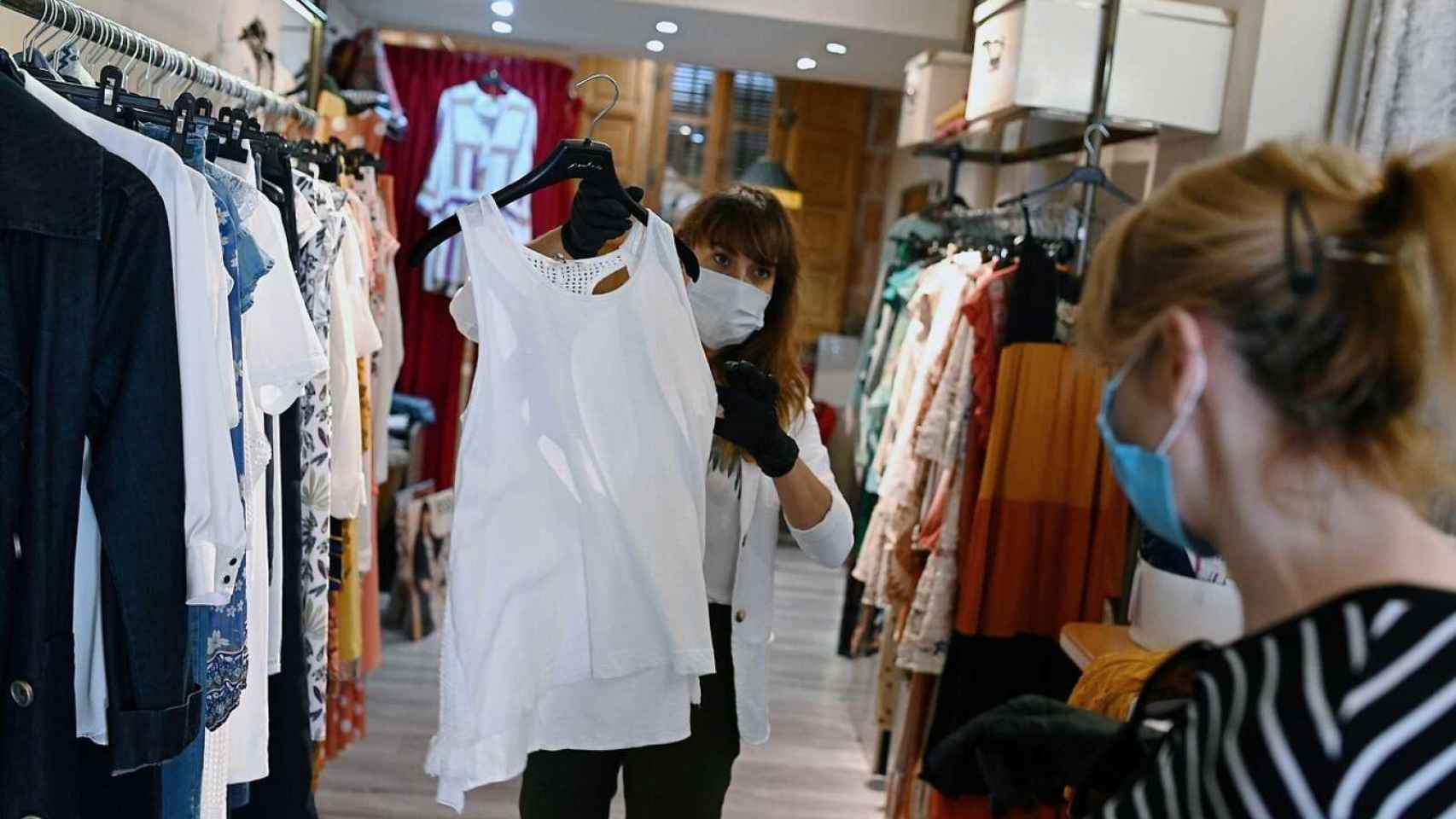 Una dependienta de una tienda de ropa muestra una prenda a una clienta / EFE