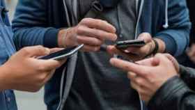 Jóvenes sujetan sus teléfonos móviles / EFE