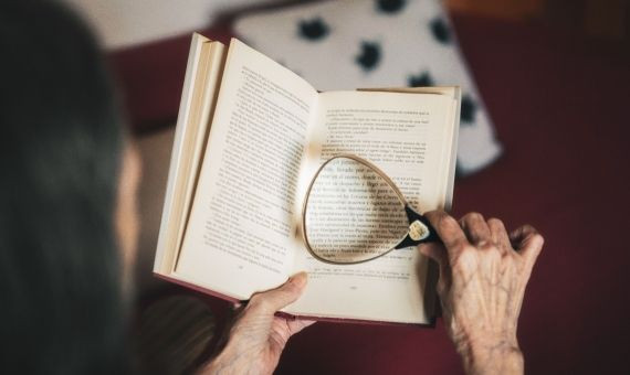 Una persona mayor lee un libro con una lupa / ARCHIVO