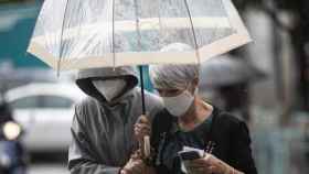 Dos personas pasean por la calle con paraguas y mascarilla / EUROPA PRESS