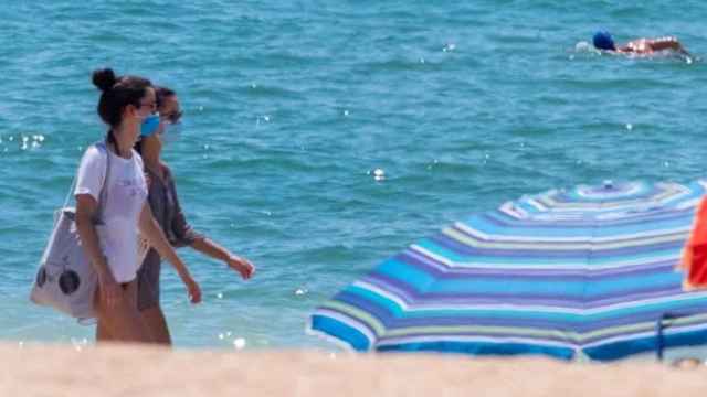 Dos chicas en la playa y con mascarilla en un día de calor / EFE