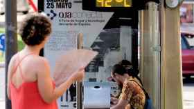 Varias personas esperan en una estación de autobús mientras el termómetro indica una temperatura superior a los 40ºC / EFE