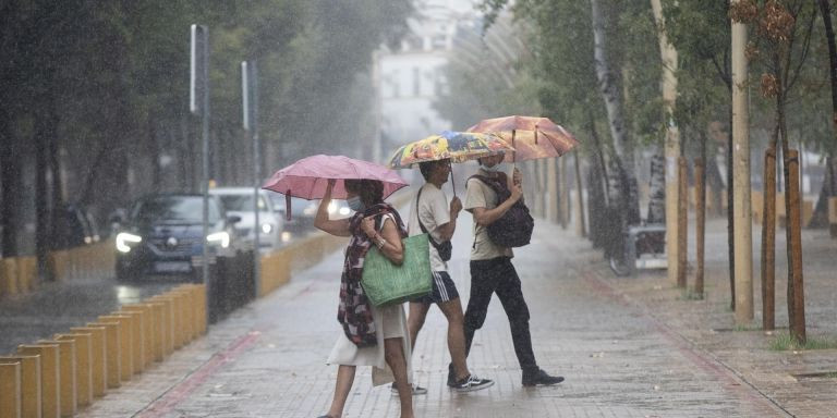 Una mujer y dos jóvenes pasean bajo la lluvia con paraguas y mascarilla durante la pandemia del covid-19 / EUROPA PRESS