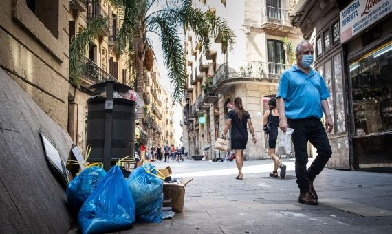 Transeúntes pasean por una calle del centro de Barcelona llena de bolsas de basura / PABLO MIRANZO - MA