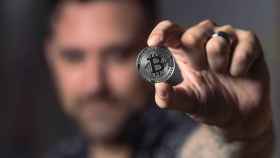 Hombre muestra una moneda con el logo de Bitcoin / PEXELS