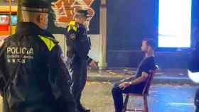 Agentes de la Guardia Urbana y Abel Azcona sentado en una silla en la Rambla / ABEL AZCONA