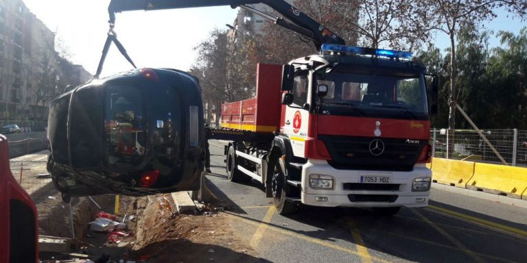 Los bomberos intervienen para sacar el vehículo volcado en una zanja de las obras de la Meridiana / BOMBERS BARCELONA