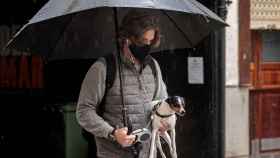 Un joven y su perro se protegen de la lluvia bajo un paraguas / EFE