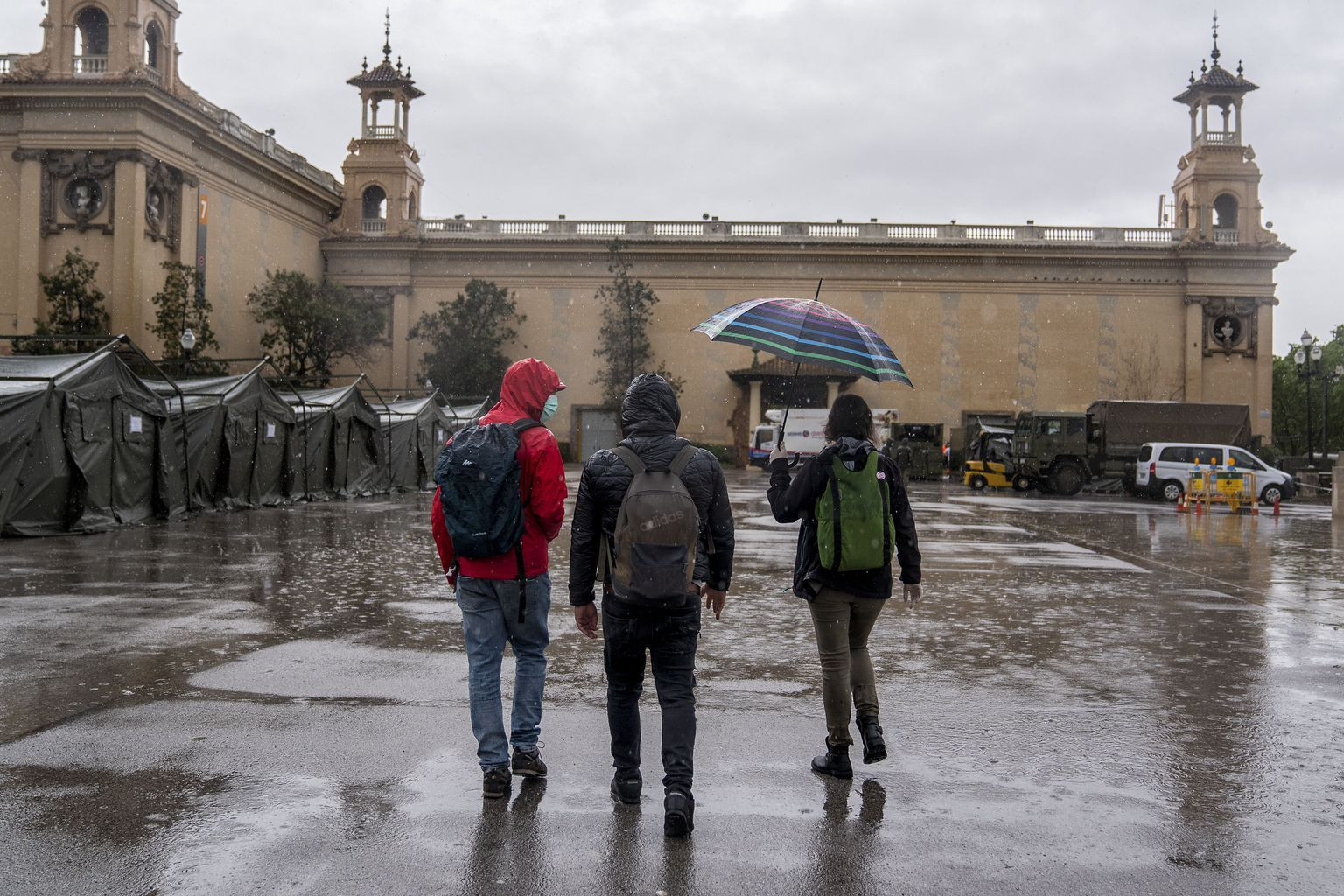 Tres jóvenes pasean bajo la lluvia en la zona de las fuentes de Montjuïc de Barcelona / AYUNTAMIENTO DE BARCELONA