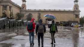 Tres jóvenes pasean bajo la lluvia en la zona de las fuentes de Montjuïc de Barcelona / AYUNTAMIENTO DE BARCELONA