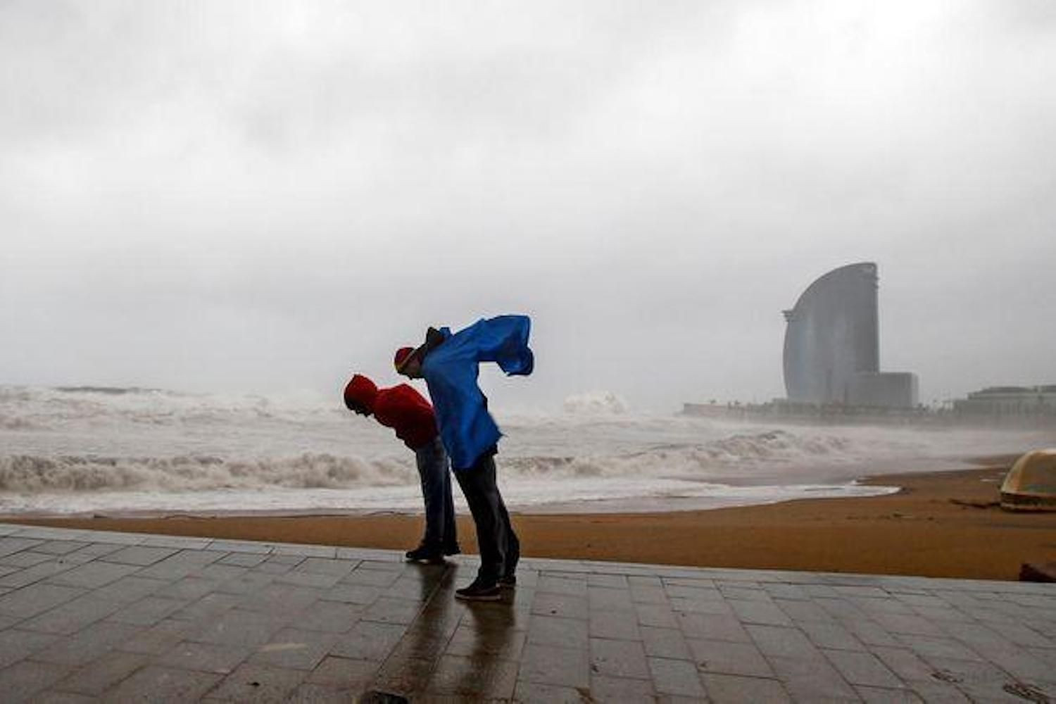 Dos personas intentan que no las tumbe el viento durante un fuerte temporal en Barcelona / EFE