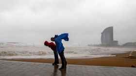 Dos personas intentan que no las tumbe el viento durante un fuerte temporal en Barcelona / EFE