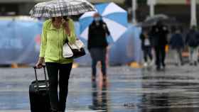 Una mujer pasea por la calle con un paraguas y una maleta en una imagen de archivo / EUROPA PRESS