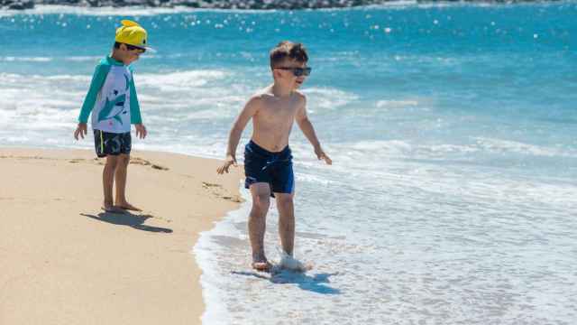 Un niño protegido con una gorra y otro con gafas de sol juegan en la playa / PEXELS